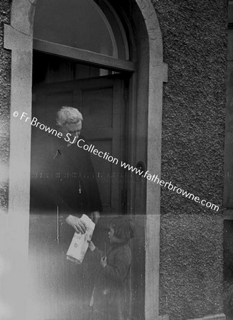 PRIEST WITH CHILD AT DOORWAY OF HOUSE